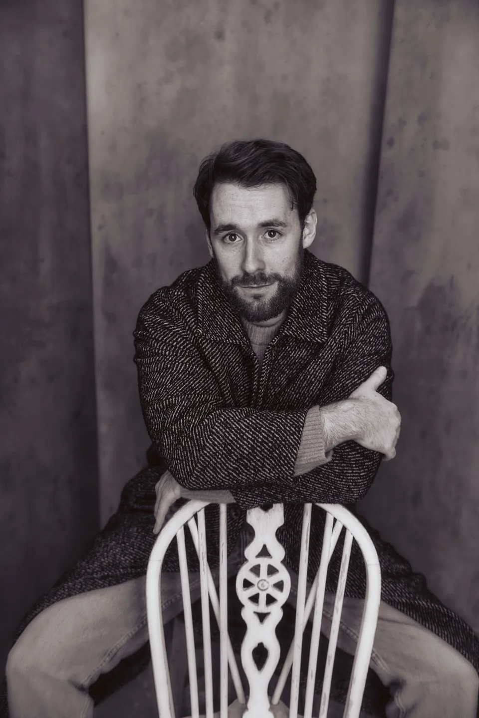 Nick Hyde in black and white, seated backwards on a wooden chair